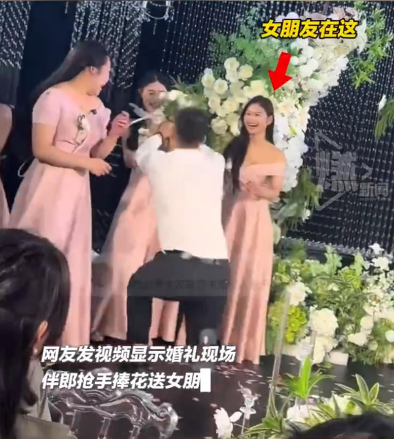 伴郎捧花求婚却跪错对象,被错跪的伴娘吓得直后退,正牌女友(红箭头处)则当场大笑。(视频截屏)