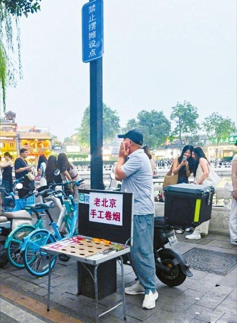 一名女子手里举着手写的广告牌和客片，胸前挂着微信支付收款码，胳膊上挂着拍立得相机，正冲着过往人群招揽生意。（取材自北京日报）