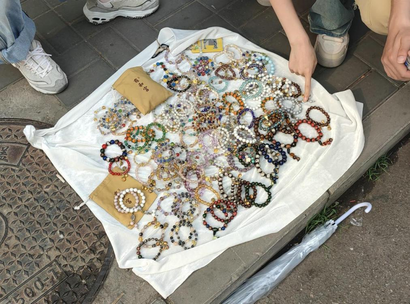 一名女子手里举着手写的广告牌和客片，胸前挂着微信支付收款码，胳膊上挂着拍立得相机，正冲着过往人群招揽生意。（取材自北京日报）