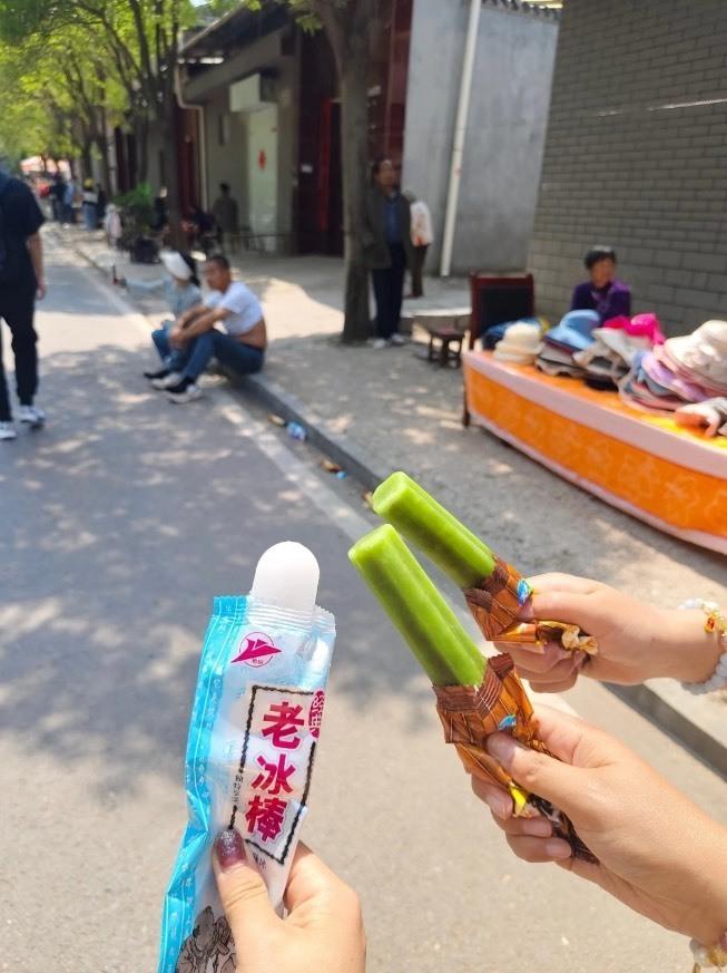 一名女子手里举着手写的广告牌和客片，胸前挂着微信支付收款码，胳膊上挂着拍立得相机，正冲着过往人群招揽生意。（取材自北京日报）