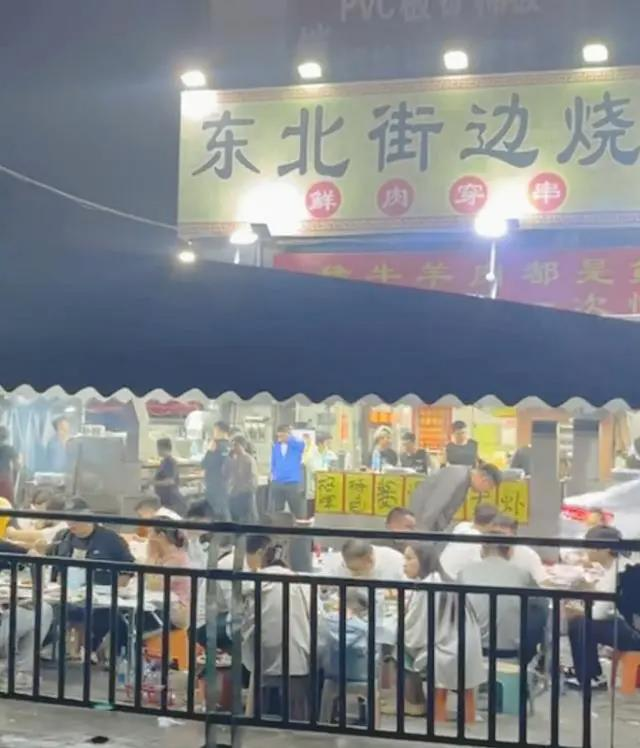 球场边的广告牌中，夹在一众高端大气的知名赞助商中的，是「东哈·东北街边烧烤」的大排档广告牌。(取材自极目新闻)