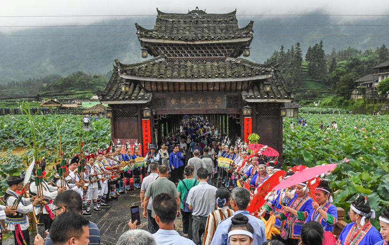 暑假到来,中国各地纷推出消费券、票价优惠、消费满减、折扣套餐等优惠措施,大抢暑假商机。图为广西三江侗族自治县的侗族文化长廊前,村民吹奏芦笙欢迎游客。(新华社)