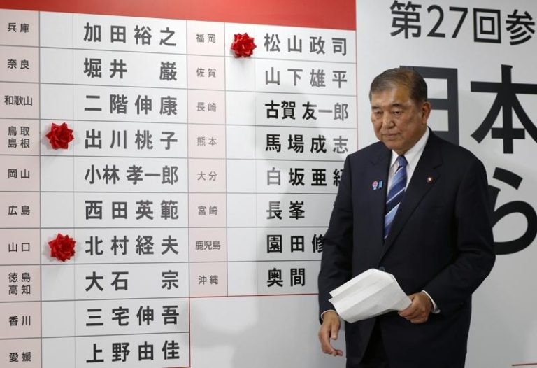 日相暨执政党自民党总裁石破茂20日在东京自民党总部，走过一块贴有少数红纸花、代表当选候选人的看板。(美联社)
