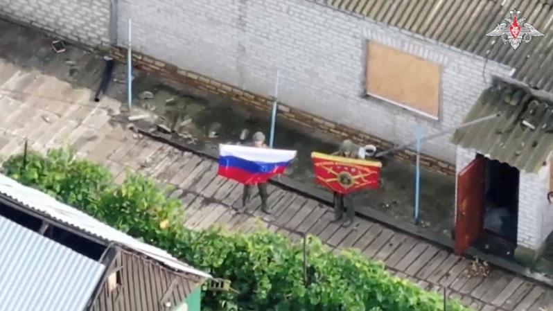 在这张取自俄罗斯国防部25日发布影像的截屏中,俄军士兵在占领乌克兰聂伯罗彼得罗夫斯克州的扎波里日凯村后展示国旗。(路透)