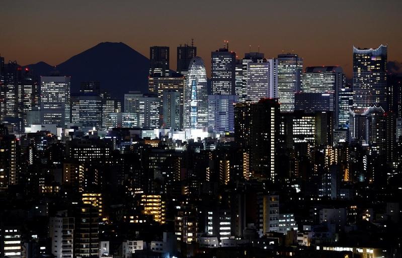 日本东京日落之后,通过东京都厅及新宿的其他摩天大楼可见富士山剪影。(路透)