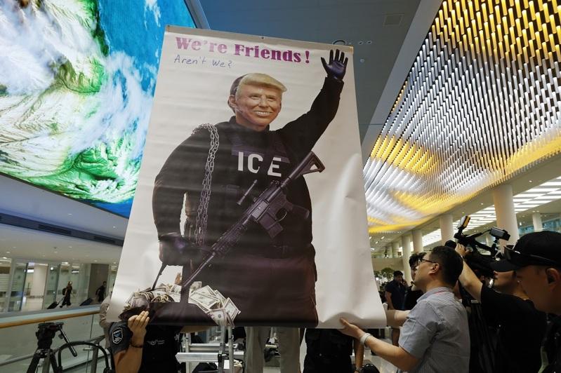 美国执法单位上周大举突袭现代汽车和LG在乔治亚州的电池工厂，当时被拘留的南韩工人12日返抵仁川国际机场之前，抗议民众举着美国总统川普身穿ICE制服的标语。（欧新社）