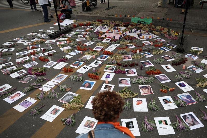 2025年11月25日,在哥伦比亚波哥大,一名示威者在纪念消除对妇女的暴力行为国际日的抗议活动中,观看被杀害女性受害者的照片。(路透)