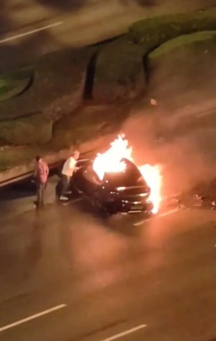 车辆起火后,一名白衣男子肘击驾驶位玻璃试图救出司机。(视频截屏)