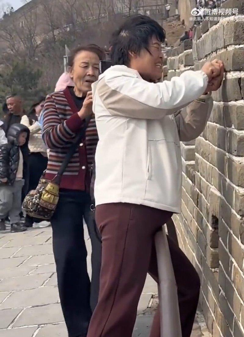 两名妇人在八达岭长城城墙上刻字。(视频截屏)