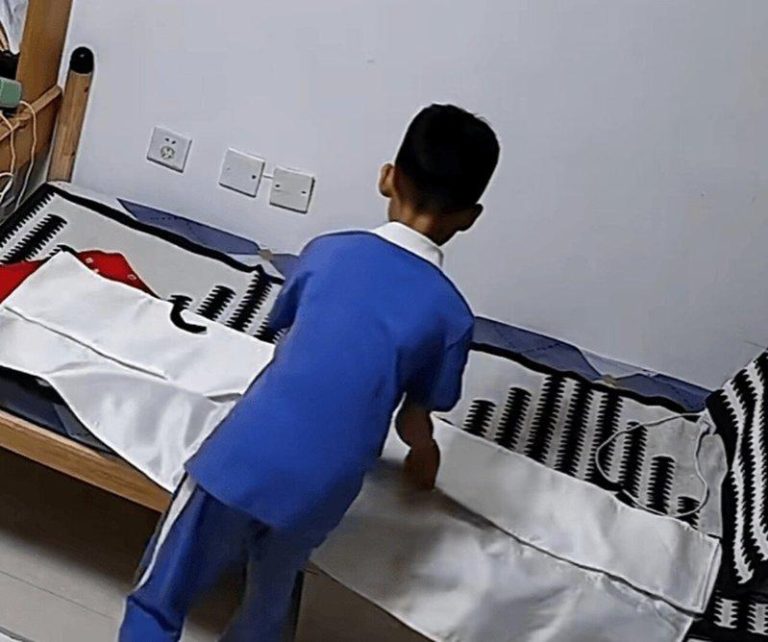 小男孩在家将灭火毯平铺在床上玩，不慎被扎。（视频截屏）