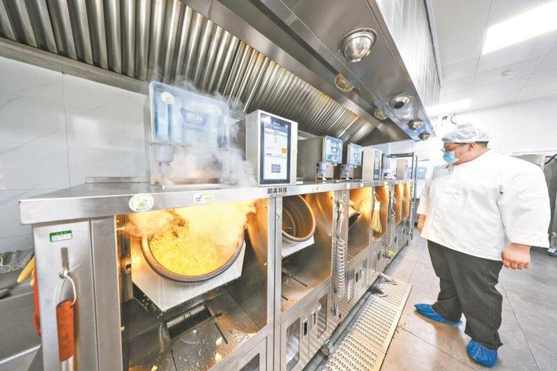 北京平谷中学食堂后厨采用「净菜+炒菜机器人」模式,一人可操作多台机器。本报北京传...