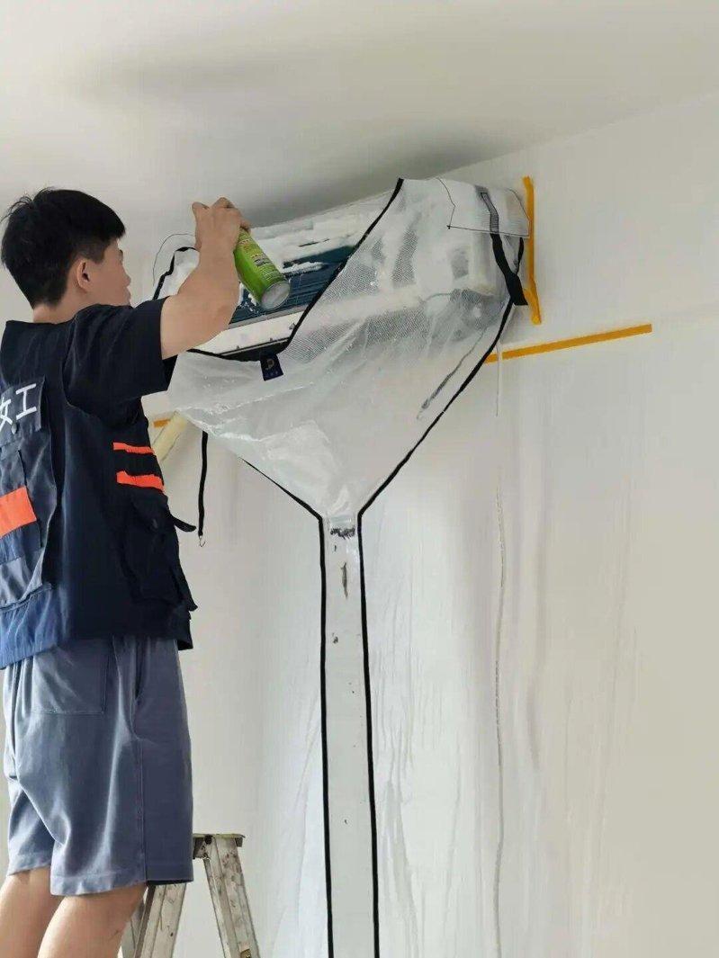 全女维修队女性工作人员在清洗空调之前,先把空调下方的墙壁贴好防护罩。 (取材自新...