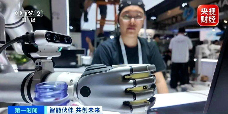 一名研发人员头戴脑电帽，靠意念操控旁边的机械臂精准抓起水杯递到面前。（取材自央视...