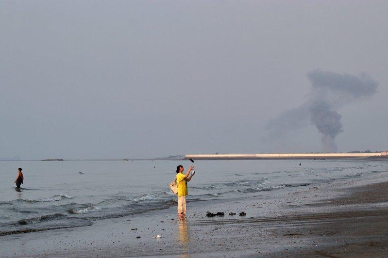 伊朗阿巴斯港附近13日发生爆炸后,远处升起一股浓烟,一名女子拿着手机站在荷莫兹海...