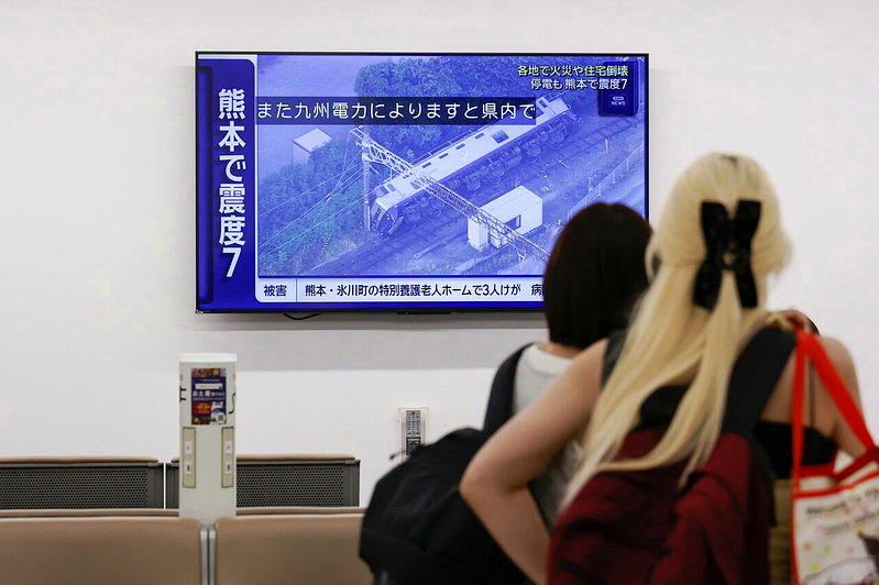 熊本28日发生规模7的浅层大地震,图为旅客在东京羽田机场观看新闻快报,机场也暂时...