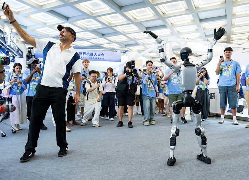 2026世界机器人大会在北京揭幕,图为人形机器人的舞姿吸引外国观众围观拍照。 (...