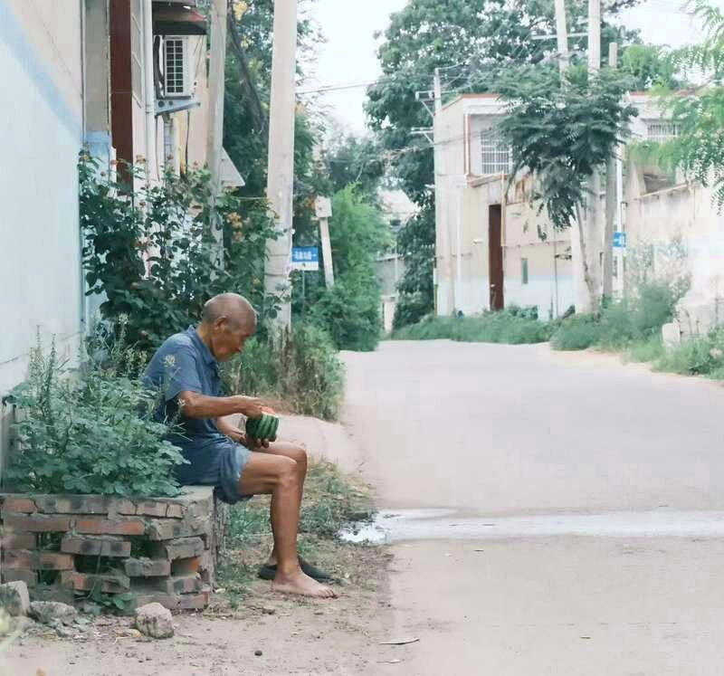 老人抱着西瓜坐在街边乘凉。（取材自新京报）