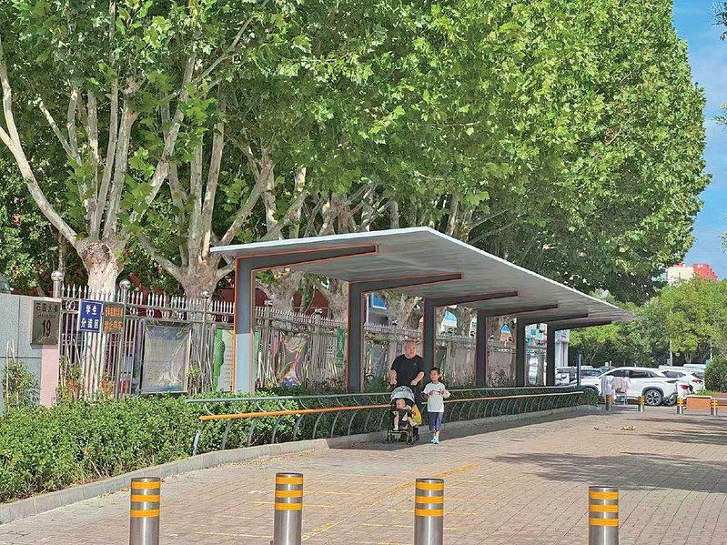 顺义石园小学门口,家长带着孩子走在长椅和遮阳棚下。这处「一根杆长椅」不仅能歇脚,...